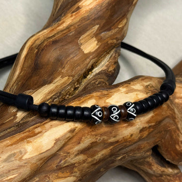 Triple black bead necklace displayed on a wooden branch, close-up of the carved beads.