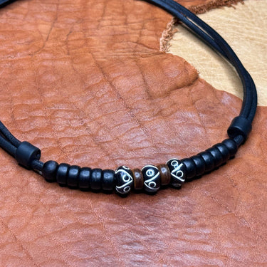 Triple black bead necklace laid on leather, showing the adjustable sliding clasp.